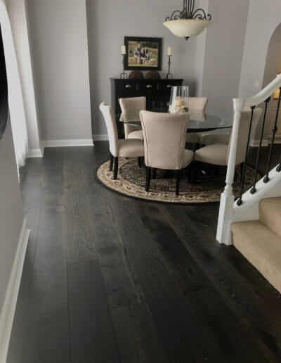 Dark-colored pre-finished hardwood flooring featured in a dining room space with grey walls and white trim.